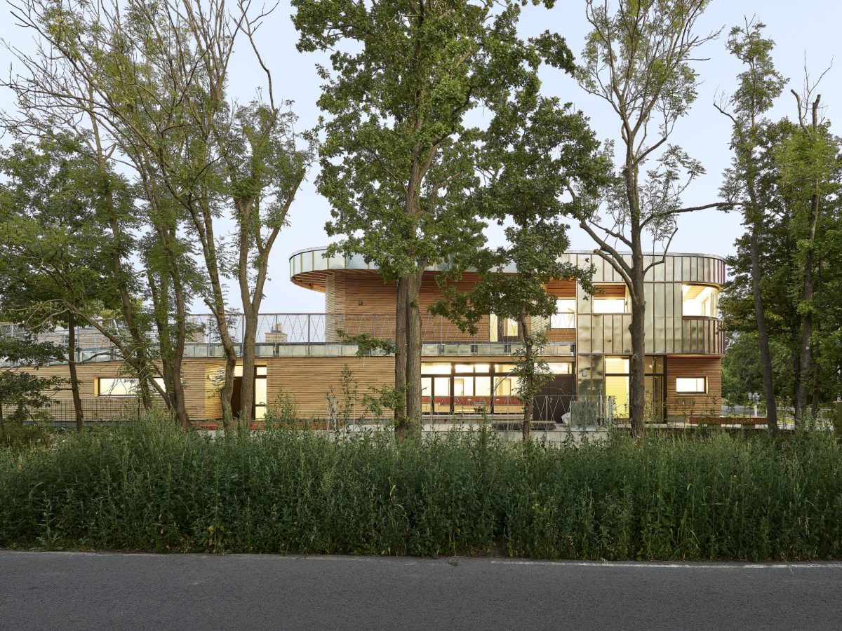 Kita mit Holz- und Metallfassade hinter Bäumen